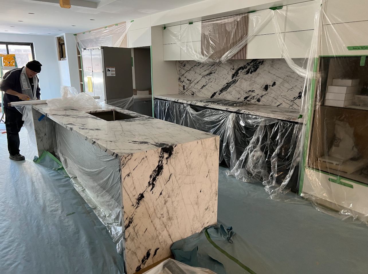 Kitchen under construction: marble island installed under protective sheeting while finish work continues